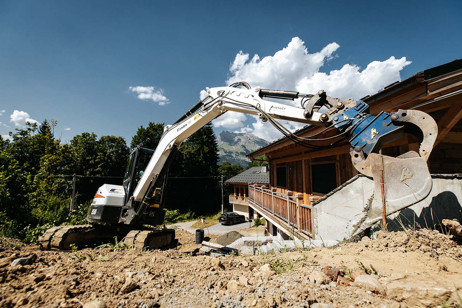 Photo d'une pelleteuse blanche entrain de réaliser un aménagement extérieur